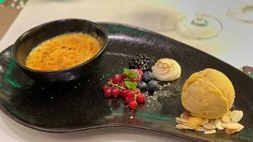 Un plato de postre con una cazuela de crema pastelera, frutos rojos y una bola de helado.
