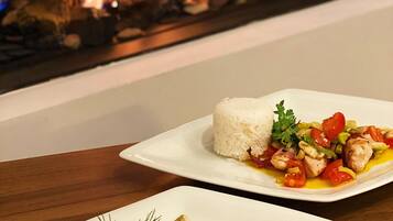 A dining table with two plates of food, one with rice and vegetables, and the other with pasta and fish, in front of a fireplace.
