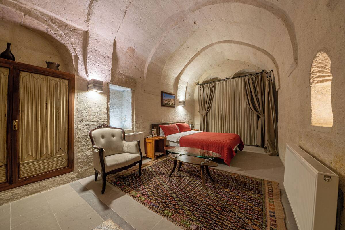 A bedroom with a bed, a chair, a table, and a window with curtains.