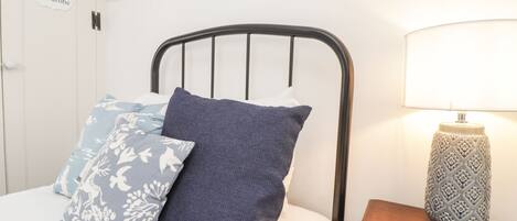 Un dormitorio con cama, almohadas, una mesita de noche con lámpara y un armario.