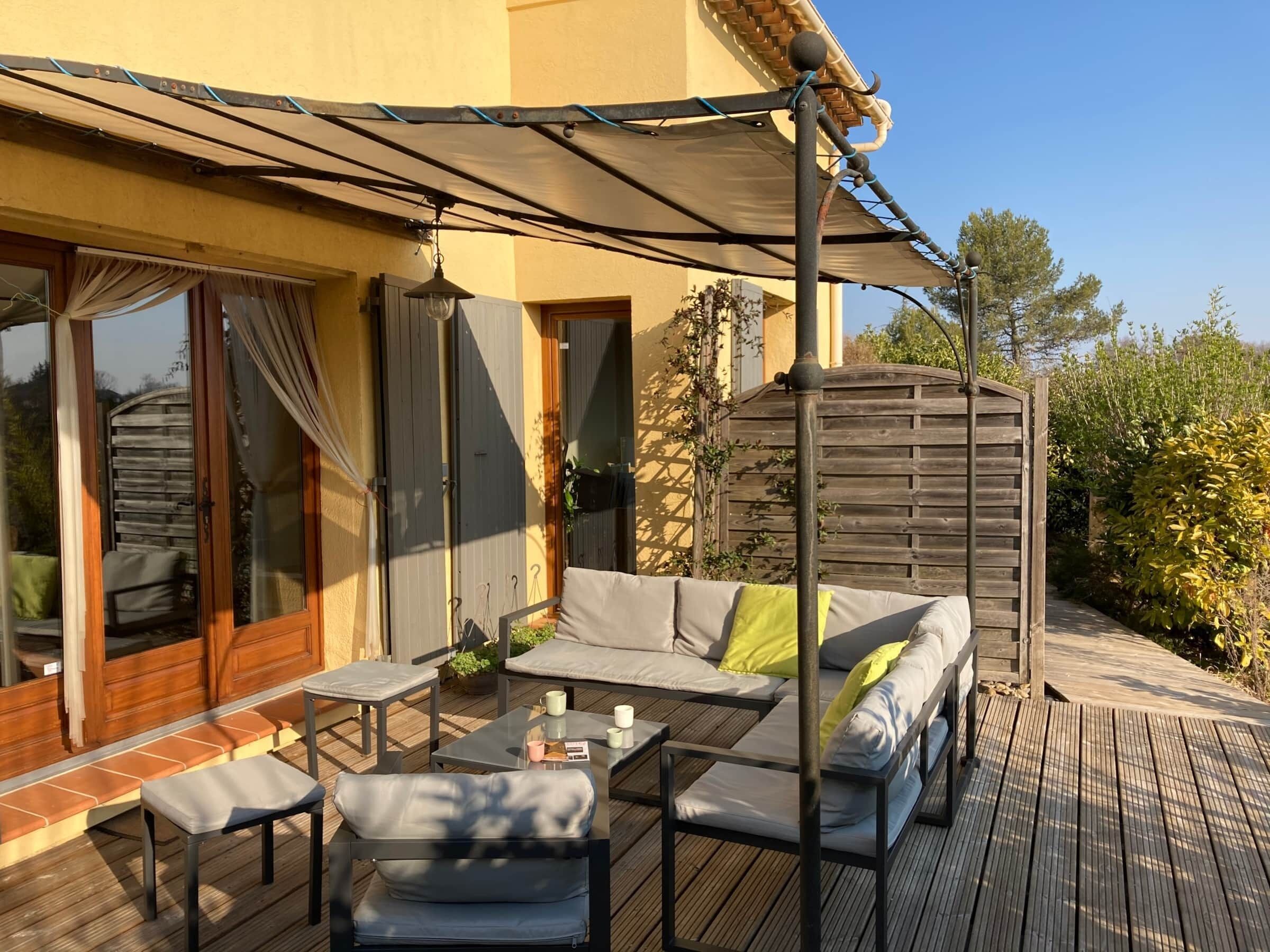 Un espace extérieur aménagé, abrité et doté d’un canapé, de chaises et de tables, d’une terrasse en bois et d’une pergola avec un toit.