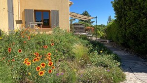 Una casa con patio, mobiliario exterior y un jardín lleno de flores.