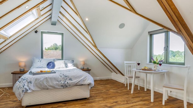 A bedroom with a sloped ceiling, a bed, a small table with a chair, and a window with a view of greenery. - 1 bedroom accommodation in Ongar (Ongar)