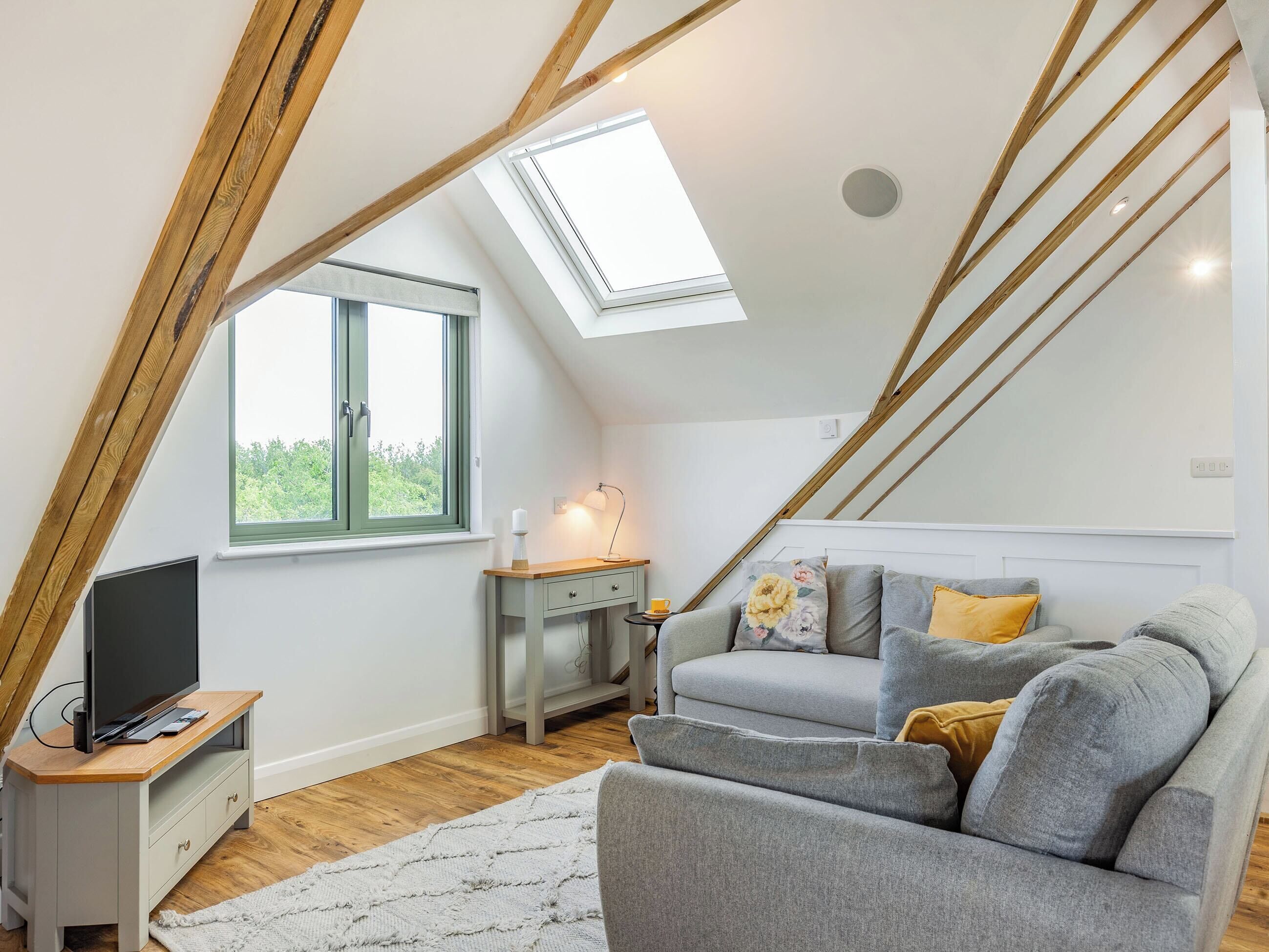 A cozy attic bedroom with a sloped ceiling, a skylight, a TV, a bedside table, and a sofa.