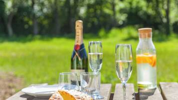 A picnic setup with a cake, champagne, and a bottle of lemonade on a wooden table.