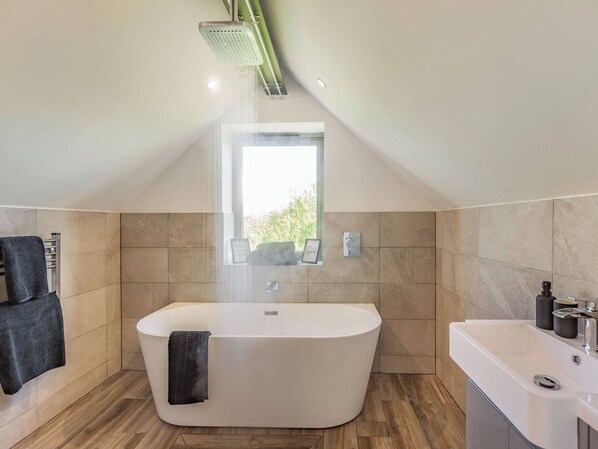 A modern bathroom with a freestanding bathtub, a showerhead, a window, and a sink with toiletries. - 1 bedroom accommodation in Ongar (Ongar)
