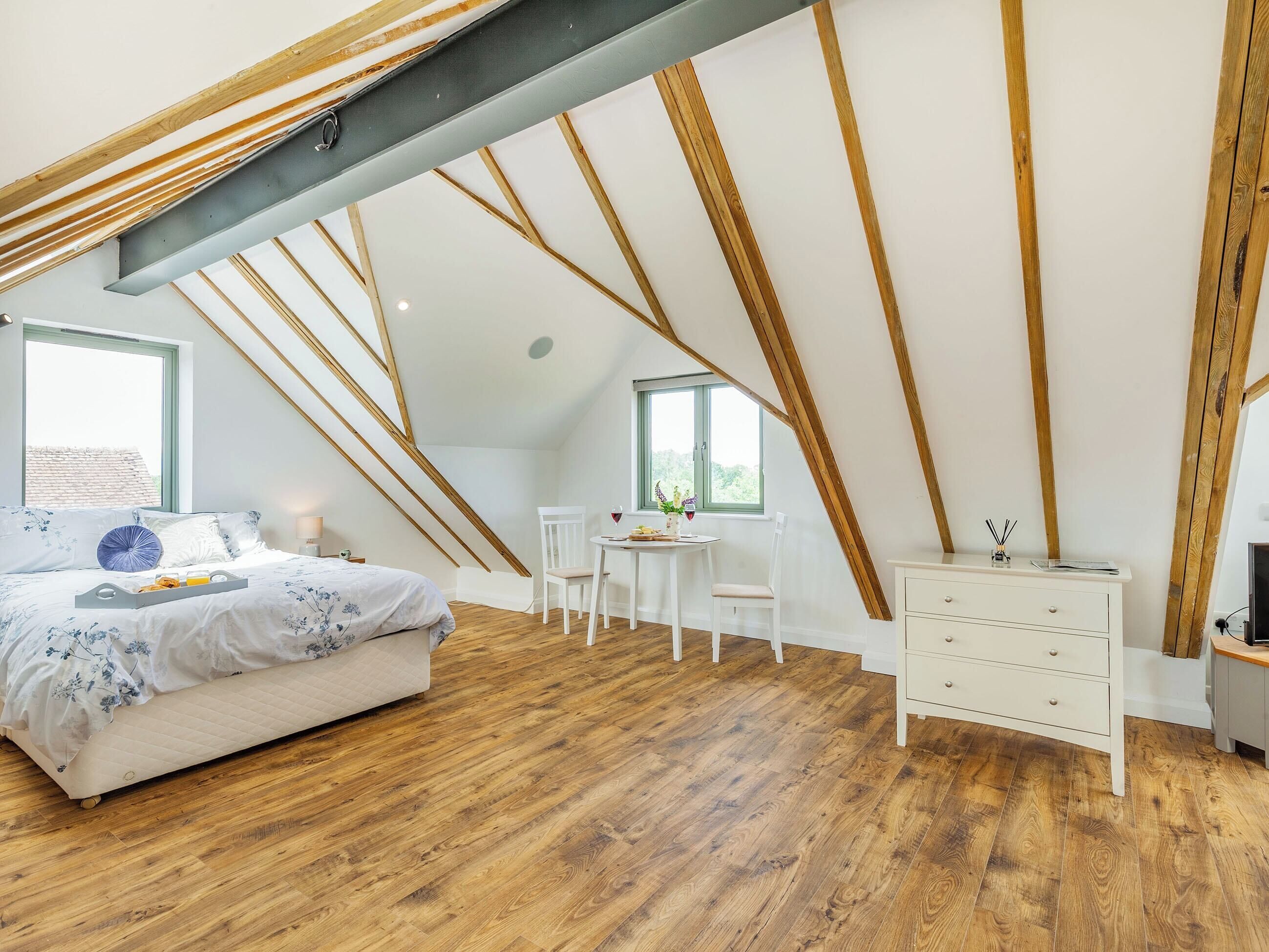 Une chambre avec un plafond en pente, des poutres en bois, un lit avec un plateau de petit-déjeuner, une petite table avec des chaises et une commode.