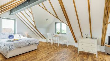 Une chambre avec un plafond en pente, des poutres en bois, un lit avec un plateau de petit-déjeuner, une petite table avec des chaises et une commode.