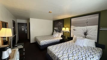 A hotel room with two beds, a desk with a lamp, a television, and a painting on the wall.