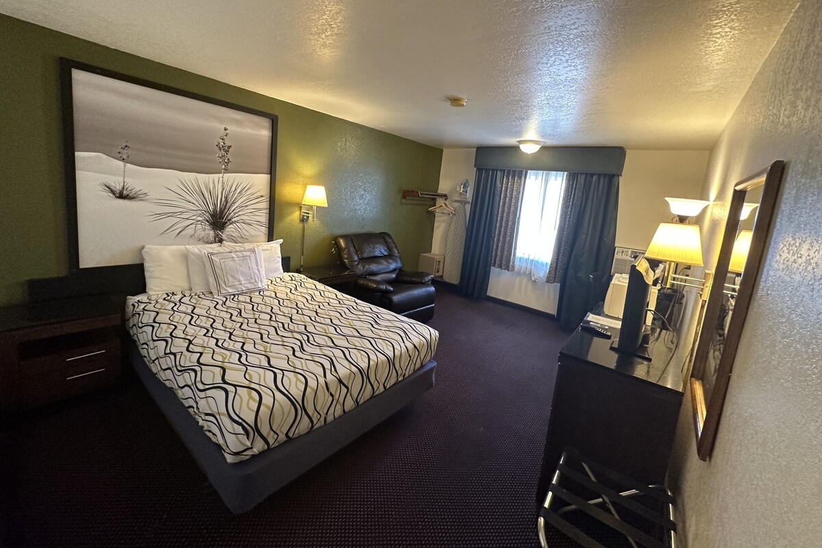 A hotel room with a bed, a chair, a desk, and a large window with curtains.