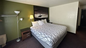 A hotel room with a bed, a nightstand, a lamp, and a painting on the wall.