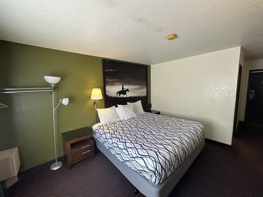A hotel room with a bed, a nightstand, a lamp, and a painting on the wall.
