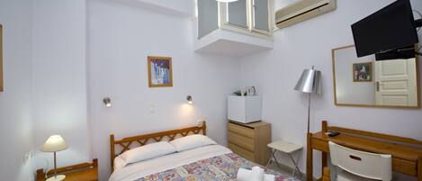 A bedroom with a bed, bedside table, desk, chair, mirror, and a TV.