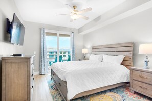A hotel room with a bed, a desk, a television, a ceiling fan, and a window with curtains.