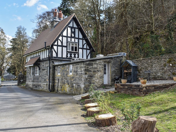 A traditional stone building with a black and white exterior, a small attached structure, and a gravel path with wooden stumps.