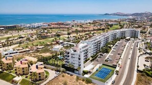 A coastal hotel with multiple buildings, a parking lot, and a tennis court.