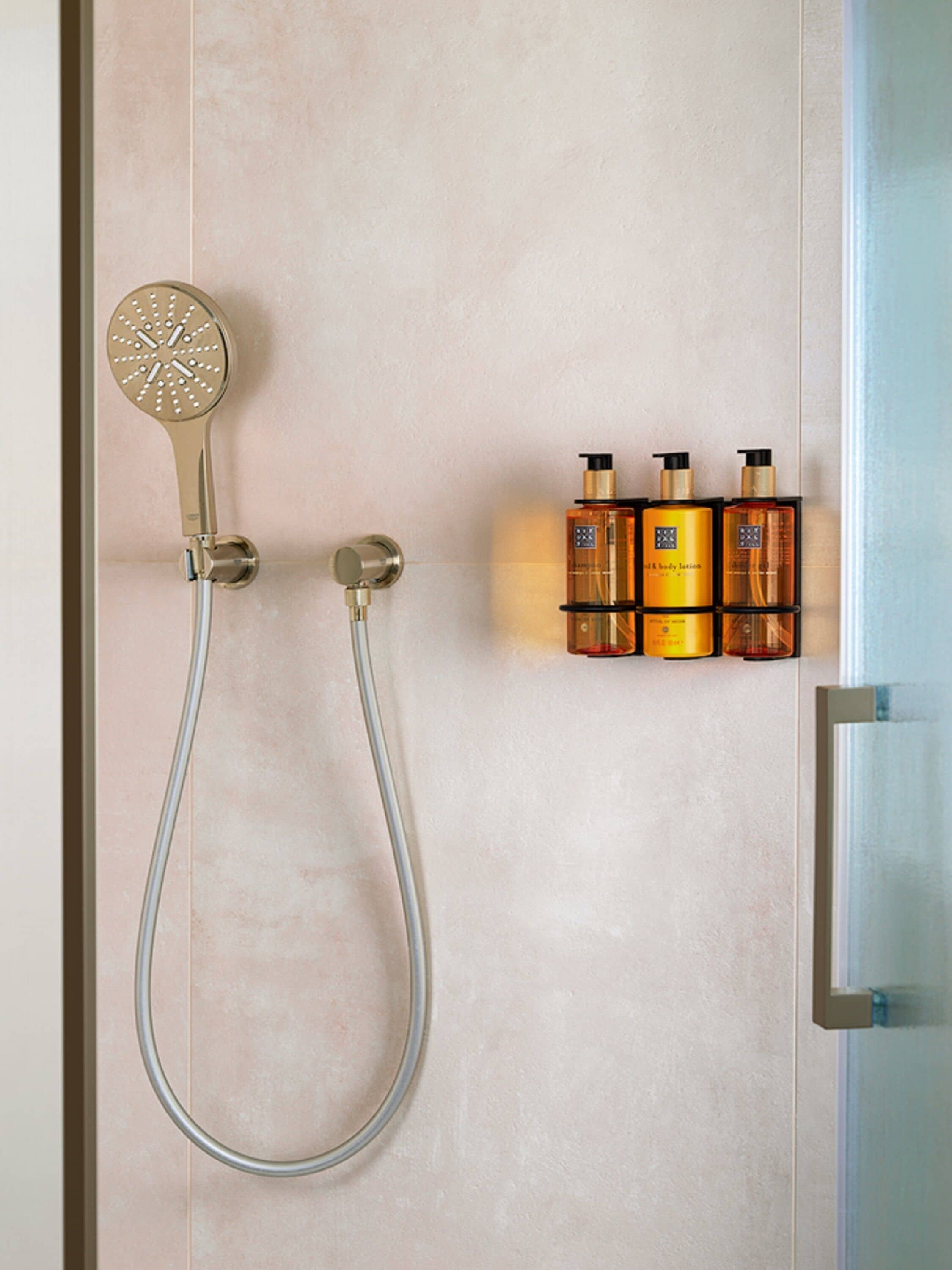 Eine Dusche mit Duschkopf und Wandarmatur, sowie drei Flaschen Flüssigseife auf einem Regal.