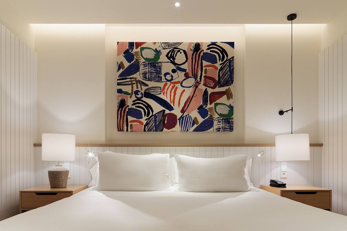 Una habitación de hotel con una cama grande, dos mesitas de noche con lámparas, un cuadro abstracto colgado en la pared y una lámpara en el techo.