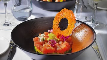 A bowl of food with a decorative orange piece on top, surrounded by empty wine glasses.