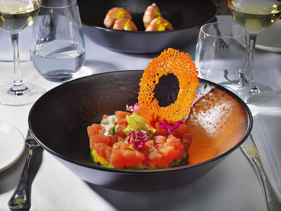 A bowl of food with a decorative orange piece on top, surrounded by empty wine glasses.