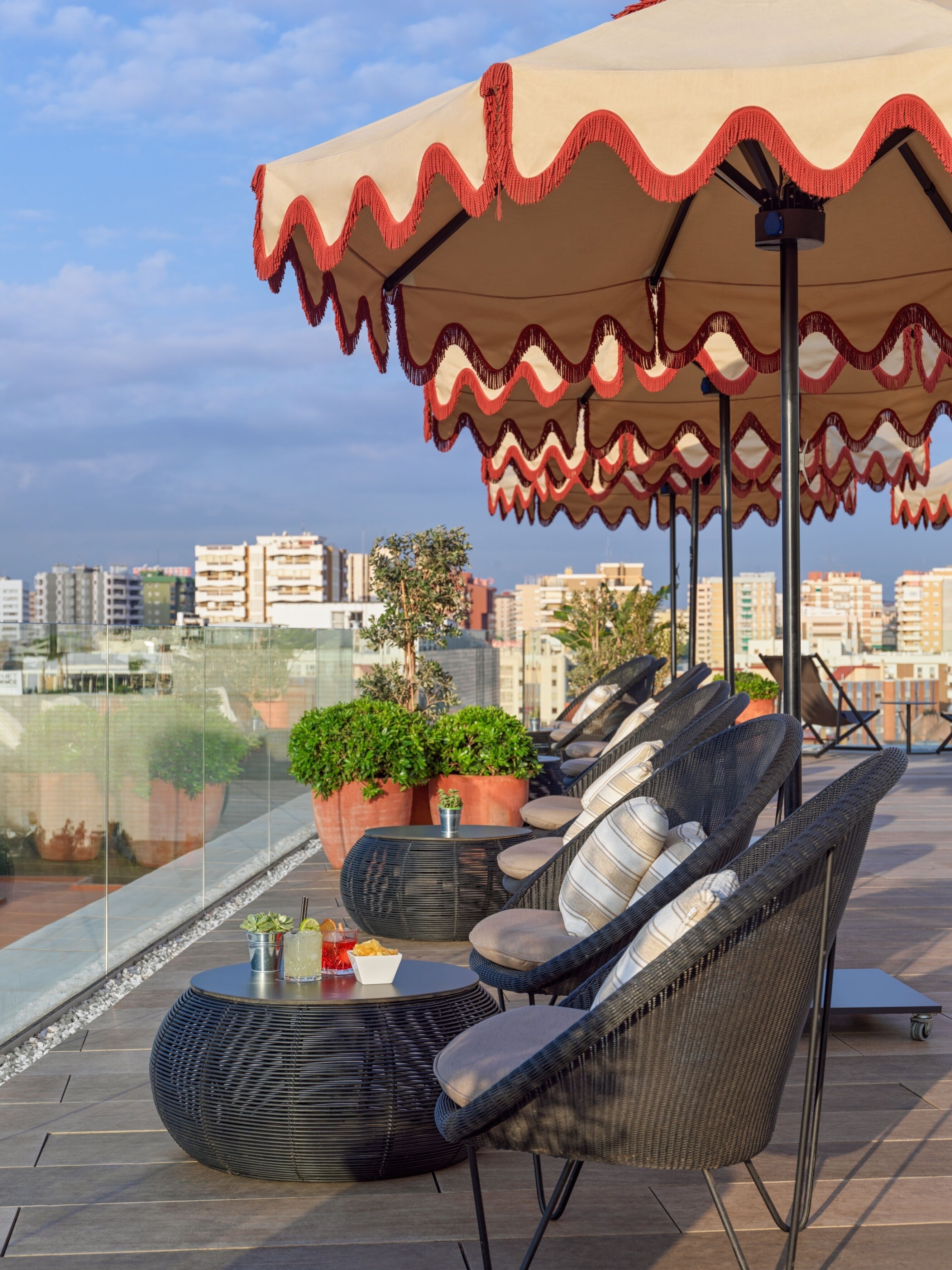 A rooftop terrace with wicker furniture, potted plants, and a view of the cityscape.