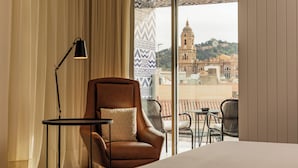 Habitación de hotel con un ventanal grande, un sillón de cuero marrón, una mesita pequeña y una lámpara.