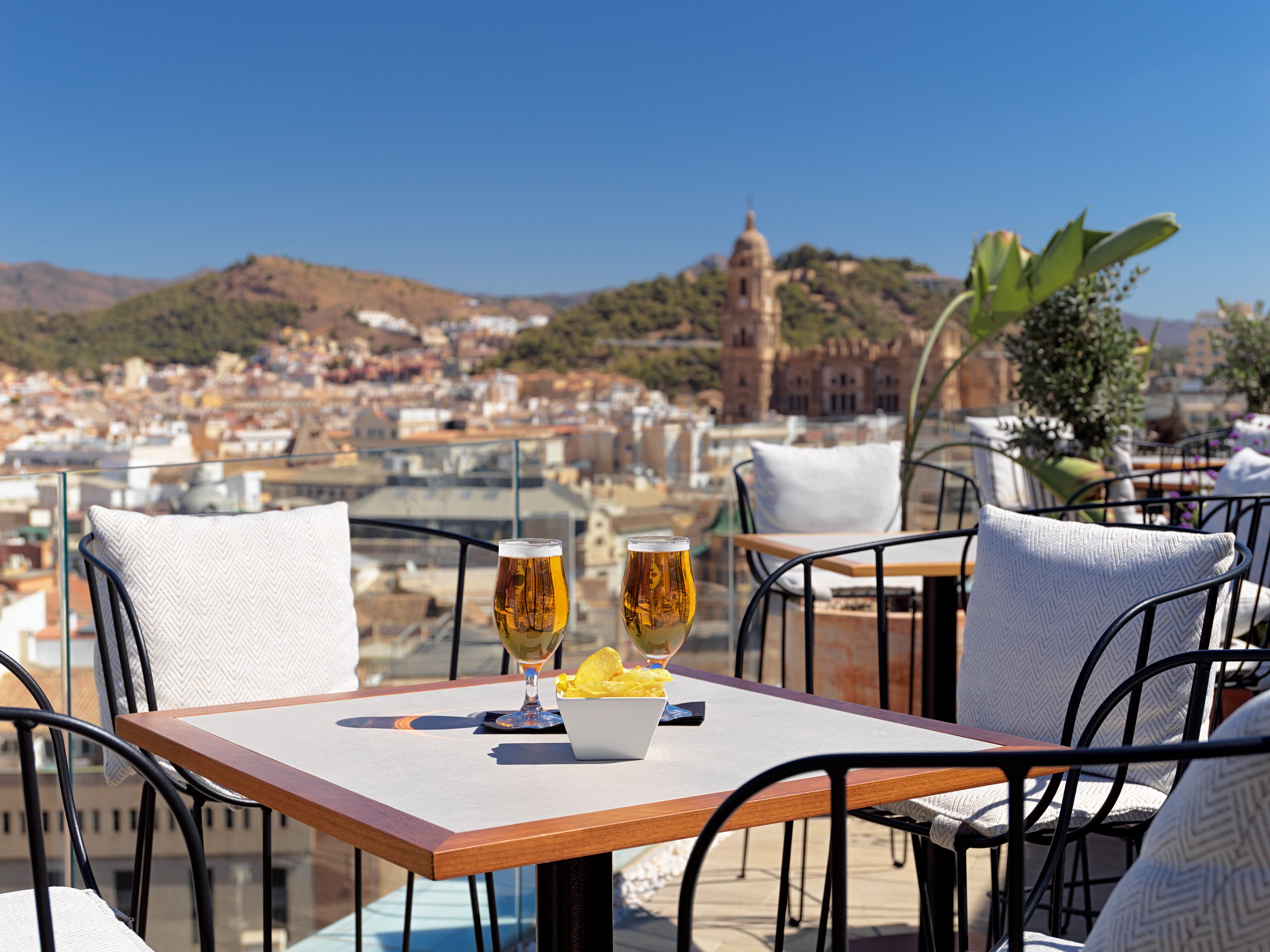 A terrace with a table set for two, two glasses of beer, and a bowl of chips.