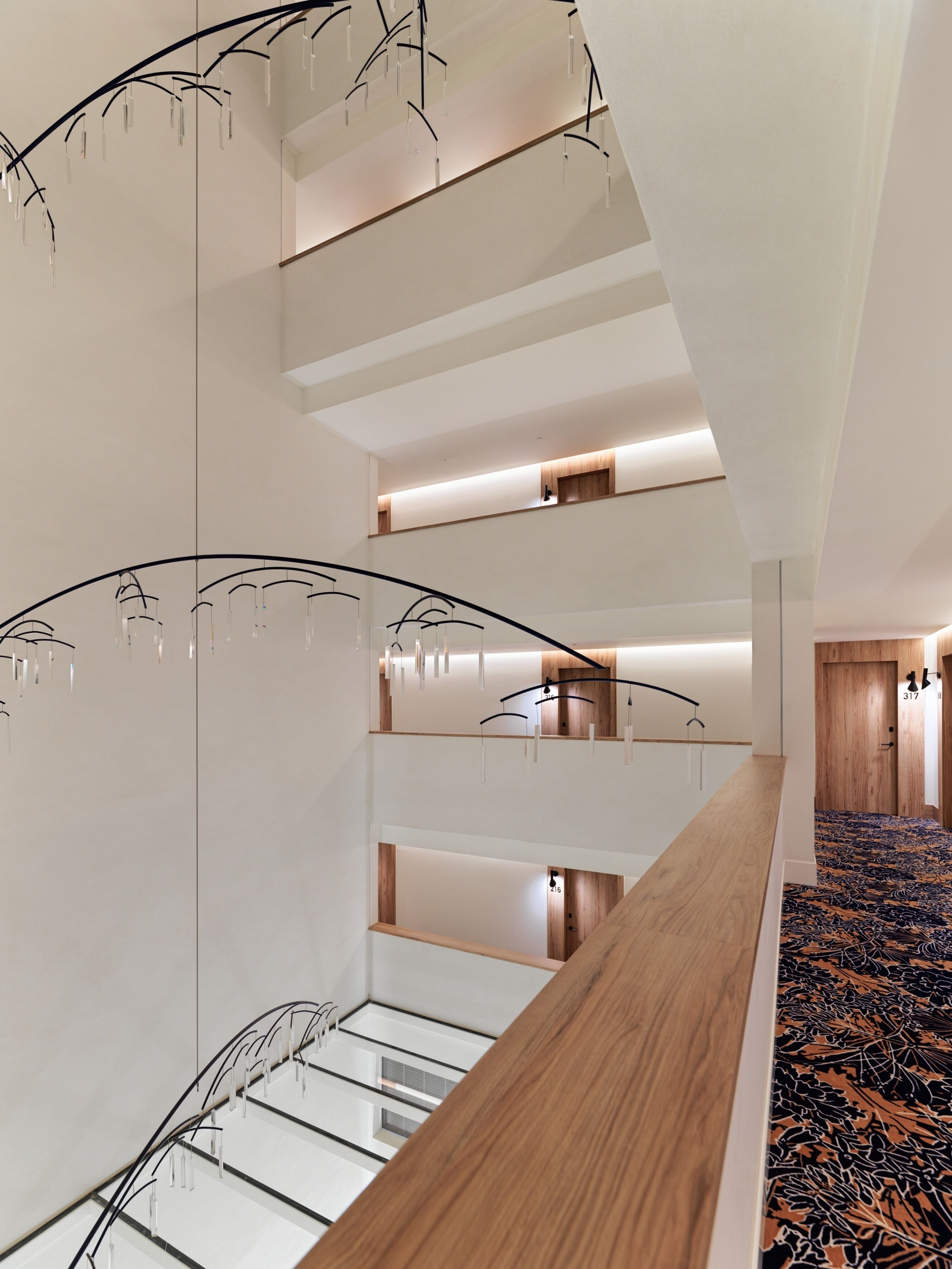 Un interior de varios niveles con una escalera central, paneles de madera y luminarias modernas.