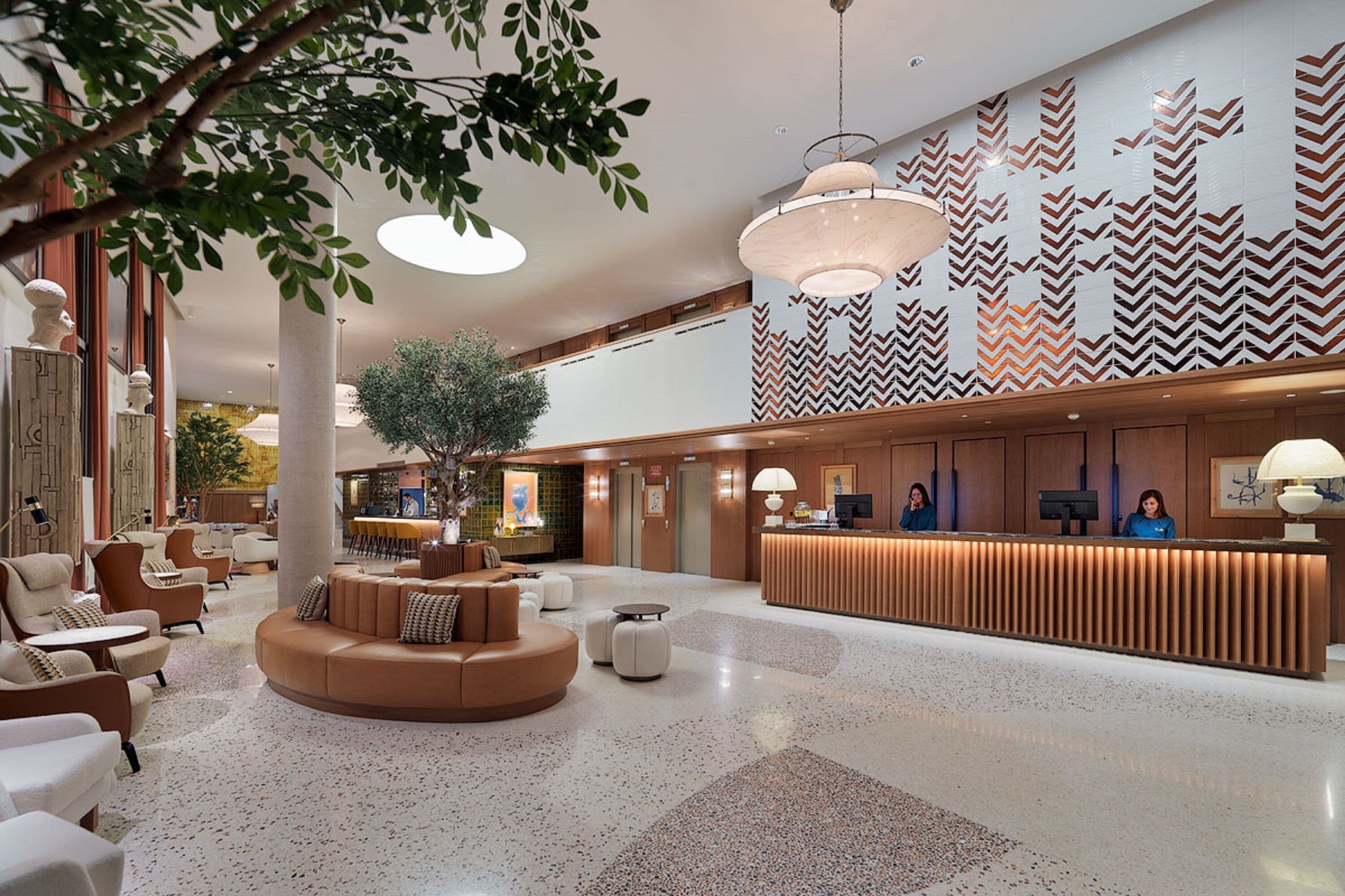 A spacious lobby with a reception desk, seating area, and a large tree.