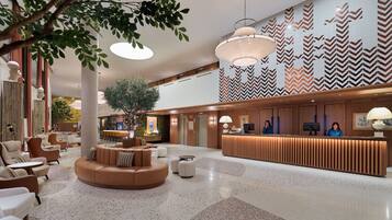 A spacious lobby with a reception desk, seating area, and a large tree.