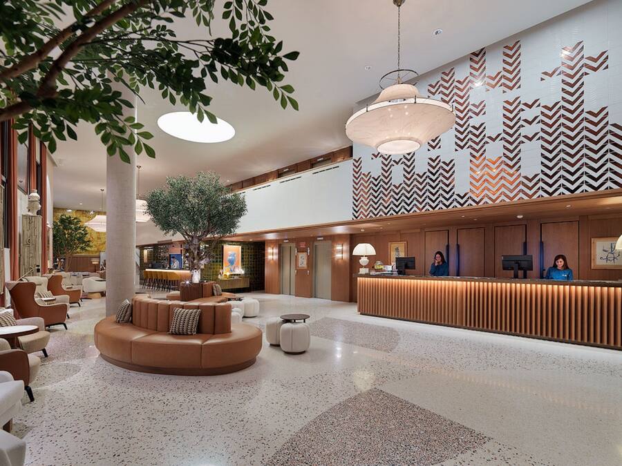 A spacious lobby with a reception desk, seating area, and a large tree.