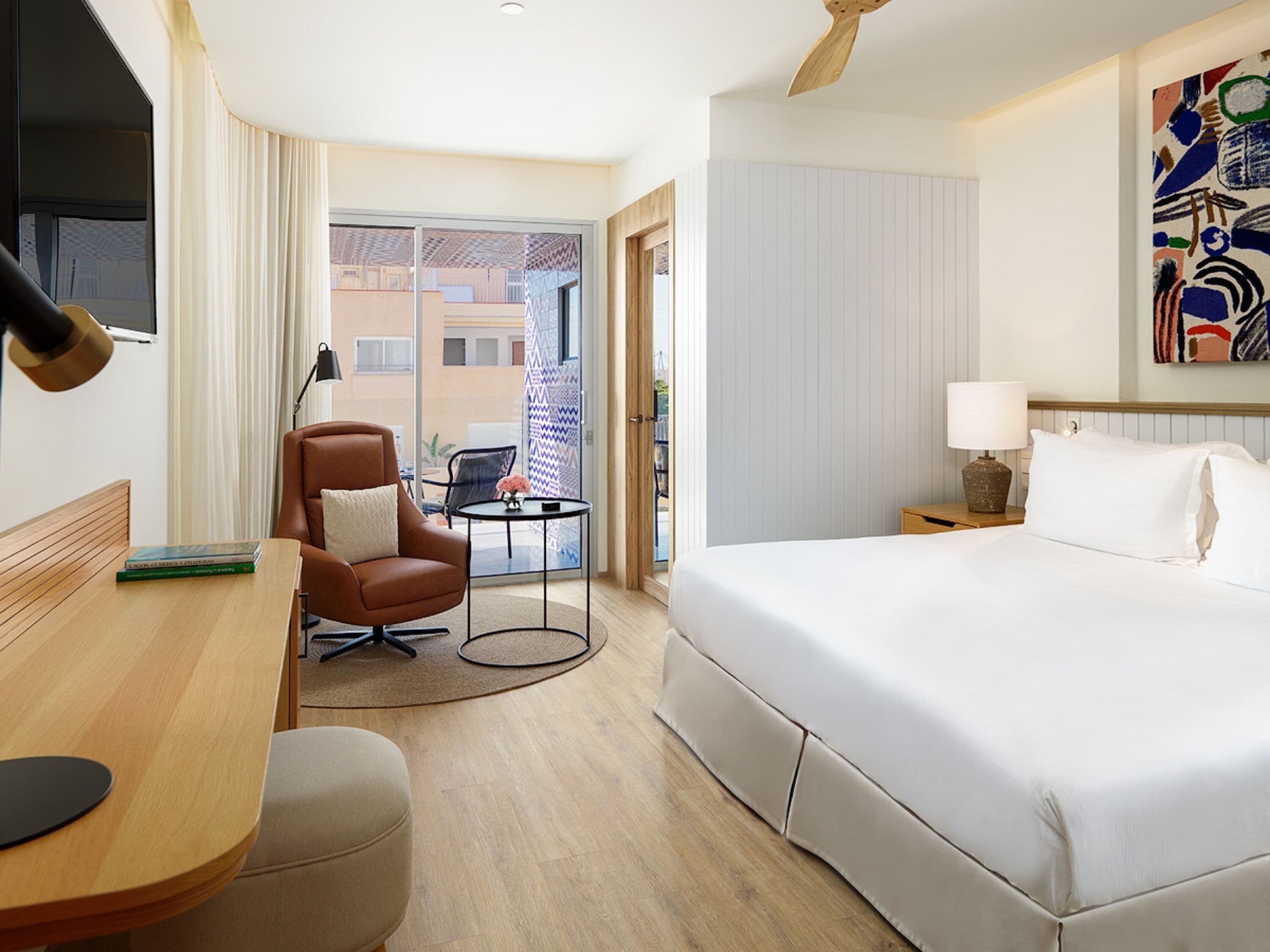 A hotel room with a bed, a desk, a chair, a small table, and a ceiling fan.