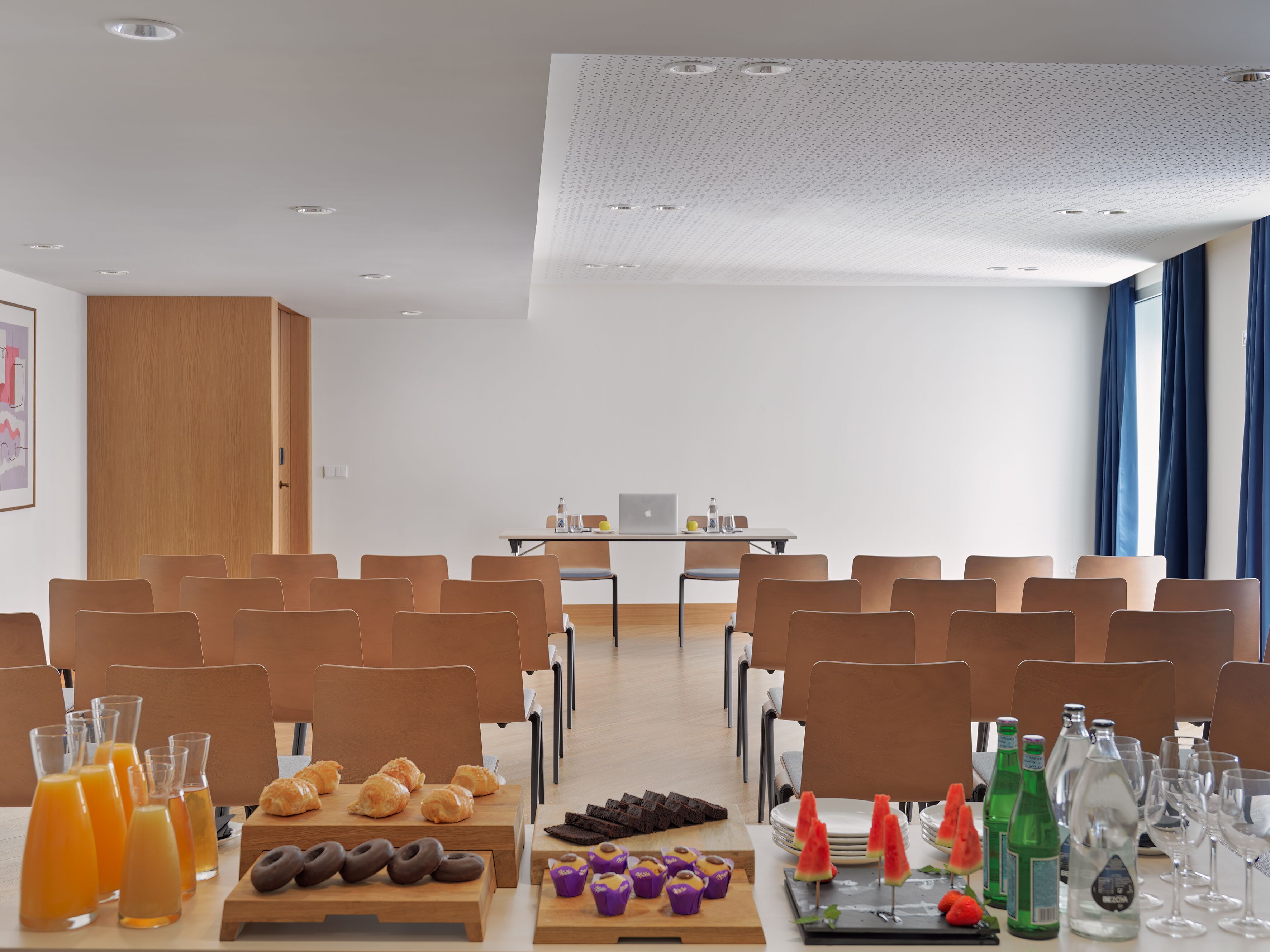 A conference room with rows of chairs, a table with breakfast items, and a laptop.