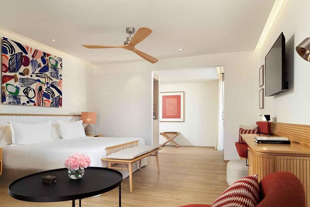 Una habitación de hotel moderna con cama, escritorio, silla, televisor y obras de arte en las paredes.