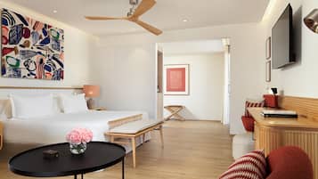 A modern hotel room with a bed, a desk, a chair, a TV, and artwork on the walls.