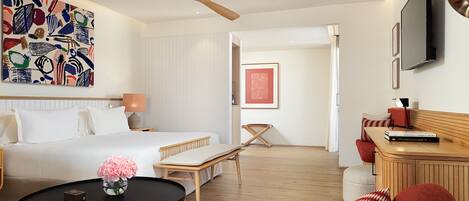 A modern hotel room with a bed, a desk, a chair, a TV, and artwork on the walls.