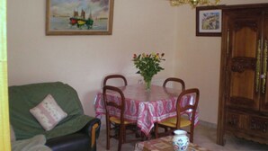 A dining area with a table set for four, surrounded by chairs, a green sofa, and a wooden cabinet. - 3 Bedroom Private vacation home in Guengat (Guengat)