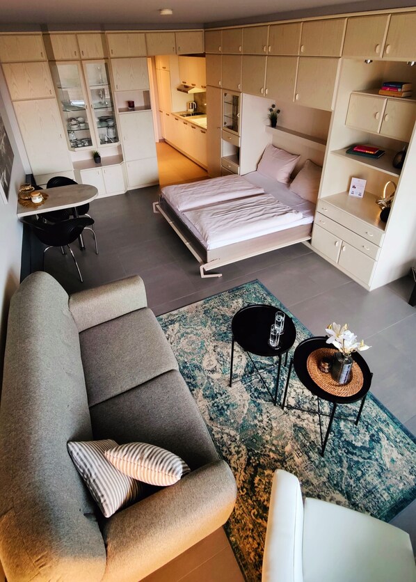 A compact studio apartment with a bed, kitchenette, and a seating area with a sofa and two side tables. - Appartment Waldidyll Landseite 713 (Timmendorfer Strand)