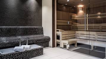Uma área de spa moderna com um banco de mosaico preto e branco, uma sauna envidraçada e bancos de madeira.