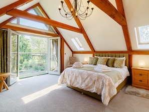 Une chambre avec un grand lit, un lustre, des poutres en bois, une vue sur l’extérieur par une porte coulissante et une petite table.