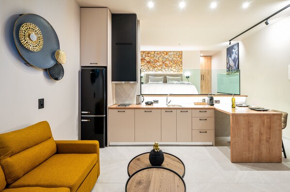 Una cocina moderna con una isla central, un comedor con un sofá amarillo y una sala de estar con una mesa de centro negra.