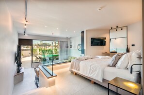 A modern bedroom with a large bed, a TV mounted on the wall, and a balcony with outdoor seating. - Pathos SeaSide Suites (Rhodes)