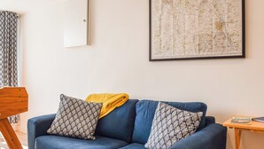 A blue sofa with patterned cushions, a wooden side table with a magazine, and a large map on the wall. - 4 bedroom accommodation in Shipston on Stour (Shipston on Stour)