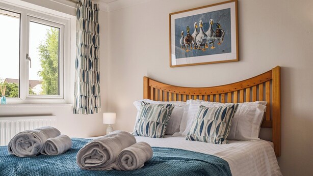 A neatly made bed with rolled towels, a wooden headboard, and a painting of ducks on the wall. - 4 bedroom accommodation in Shipston on Stour (Shipston on Stour)