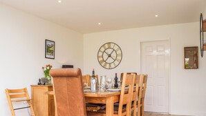 A dining area with a wooden table set for six, surrounded by wooden chairs. A large wall clock and a framed picture are visible. - 4 bedroom accommodation in Shipston on Stour (Shipston on Stour)