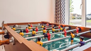 A foosball table in a room with a window and patterned curtains. - 4 bedroom accommodation in Shipston on Stour (Shipston on Stour)