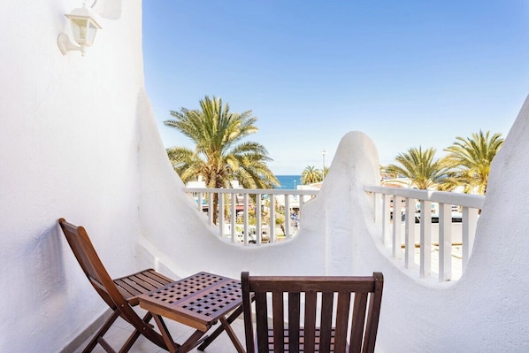 Un balcon avec une balustrade blanche, deux chaises en bois et une petite table.