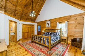 A wooden cabin bedroom with a bed, a window with curtains, a wooden ceiling, and a wooden floor.