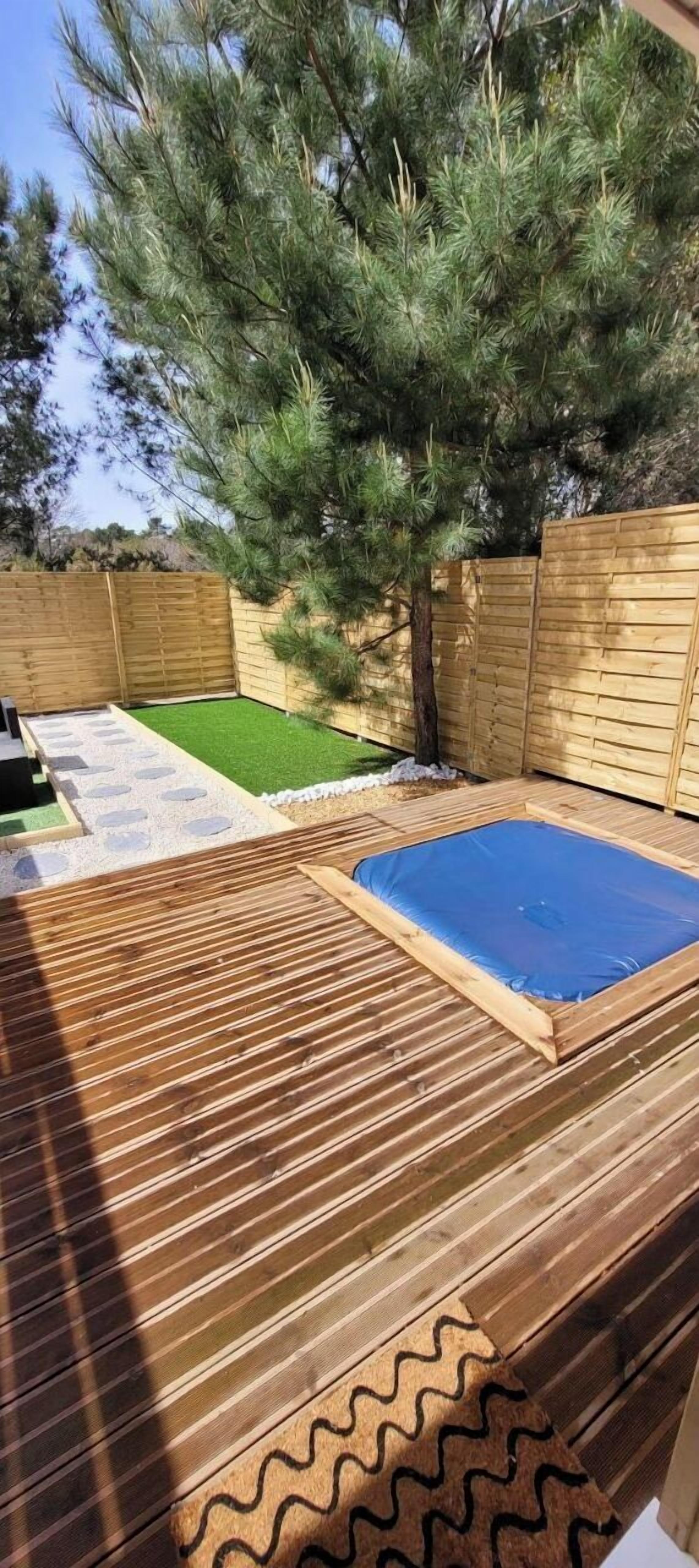 A wooden deck with a blue inflatable pool, surrounded by a wooden fence and a tree.