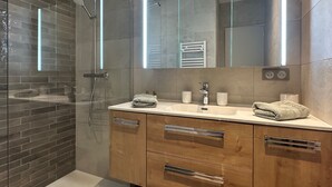 A modern bathroom with a glass shower enclosure, a vanity with a mirror, and wooden cabinetry. - Fully restored garden apartment (Saint-Tropez)